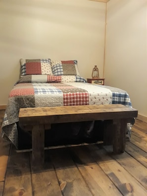 Una cama con colcha de retazos y un banco de madera adelante.