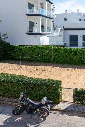 A modern building with balconies, a parked motorcycle, and a sandy area. - #425 Cozy Getaway in Albufeira | Shared Pools (Albufeira)