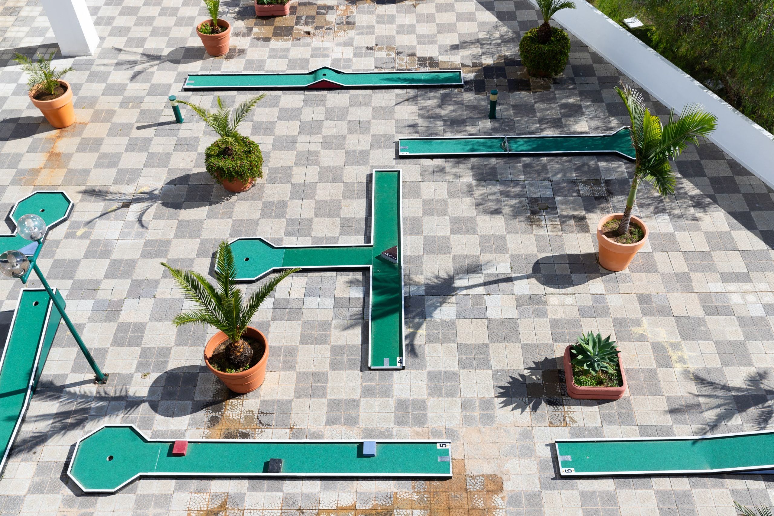 A rooftop terrace with a checkered floor, green metal railings, and potted plants.