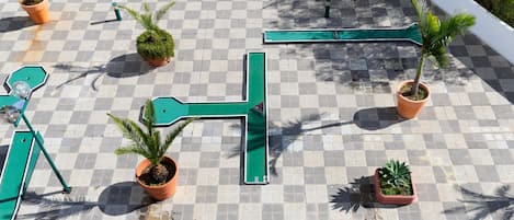 A rooftop terrace with a checkered floor, green metal railings, and potted plants.