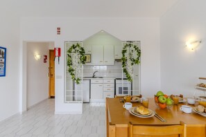 A modern kitchen with white cabinets, a built-in oven, and a dining area with a wooden table set for breakfast. - #425 Cozy Getaway in Albufeira | Shared Pools (Albufeira)