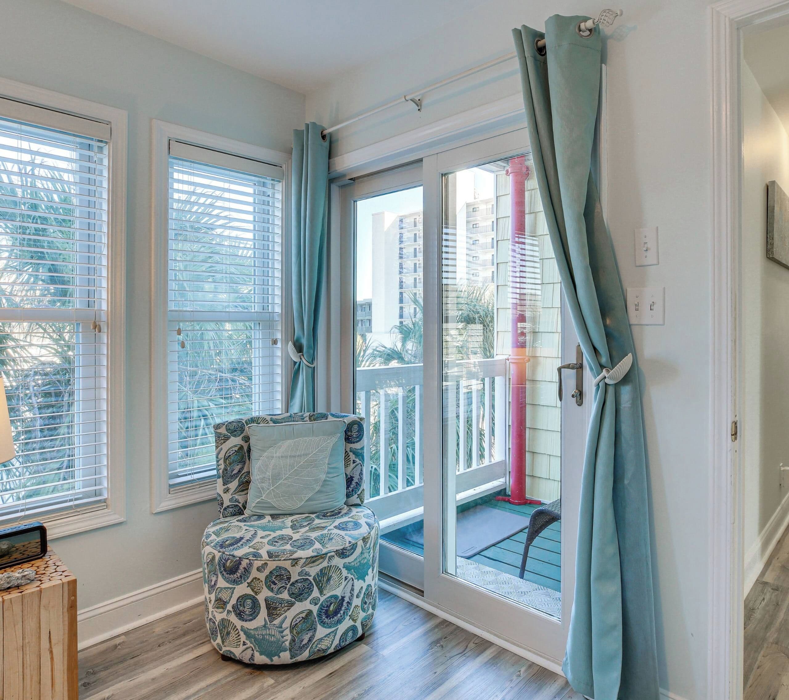 A room with a view of a balcony, a chair with a leaf pattern cushion, and a wooden side table.