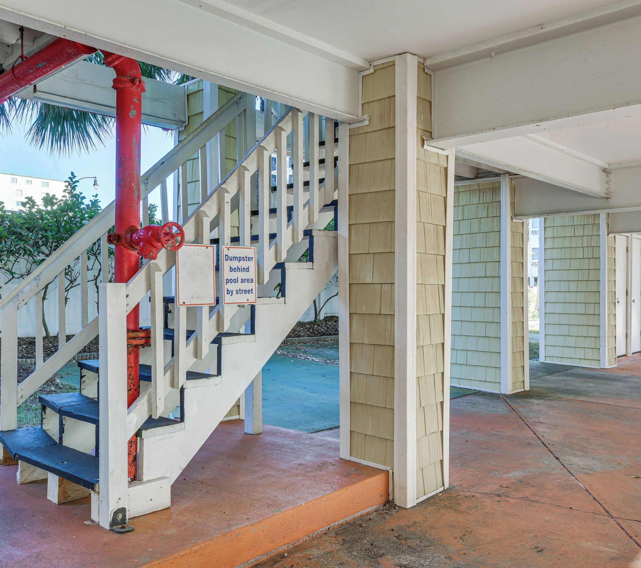 A staircase with a sign indicating a dumpster behind a pool area by the street.