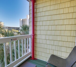 Ein Balkon mit weißer Brüstung, einer roten Rohrleitung und einem Stuhl.