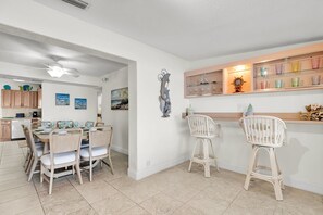 A dining area with a table set for four, a kitchen with wooden cabinets, and a bar area with a glass display case. - Sea Dreams are yours! (Marathon)