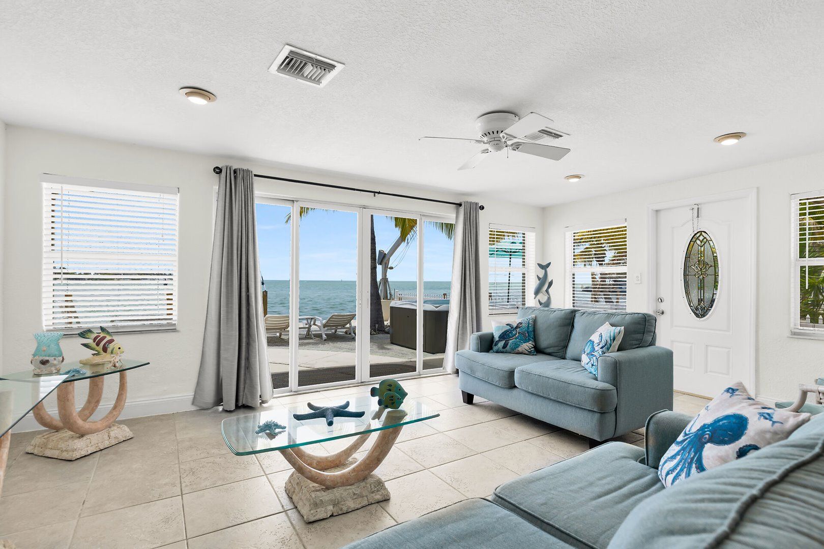 A spacious living room with a large window, a ceiling fan, and a view of the ocean.
