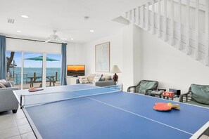Una habitación con mesa de ping pong, sofá, televisor y vista al mar.
