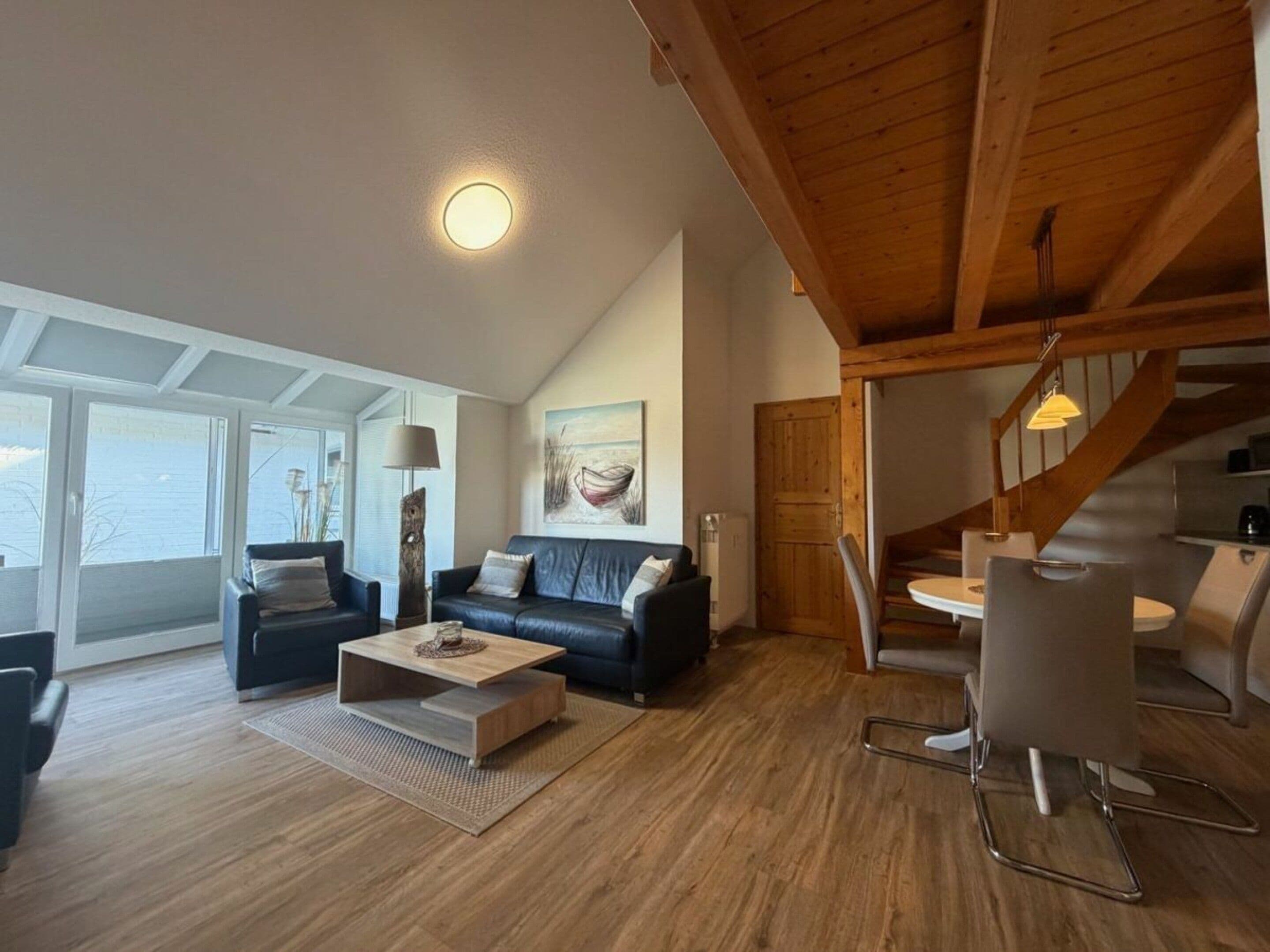 Un salon moderne avec un plafond en bois, un canapé noir, une table basse et un coin repas avec des chaises.