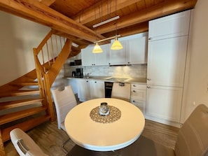 Eine Küche mit weißen Schränken, einem Esstisch mit einer Vase und einer Holztreppe.