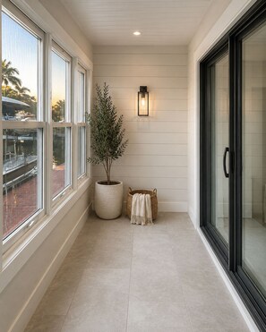 A corridor with large windows, a potted plant, a wall-mounted light fixture, and a sliding glass door. - "Hey Jude"~Longboat Key ~Waterfront Bayside Escape (Longboat Key)