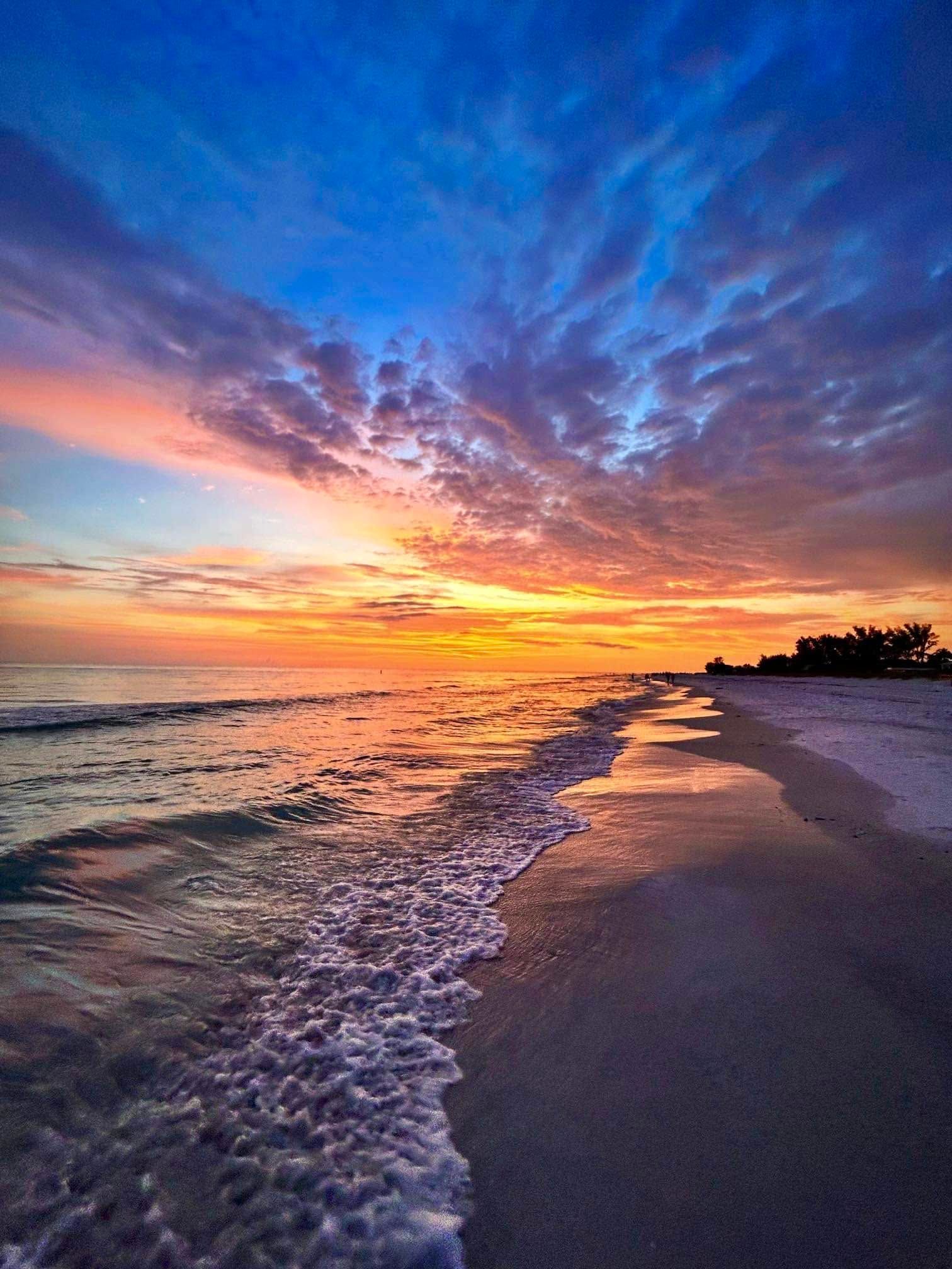 Ein Strand mit Wellen, einem Sonnenuntergang und wolkenlosem Himmel.