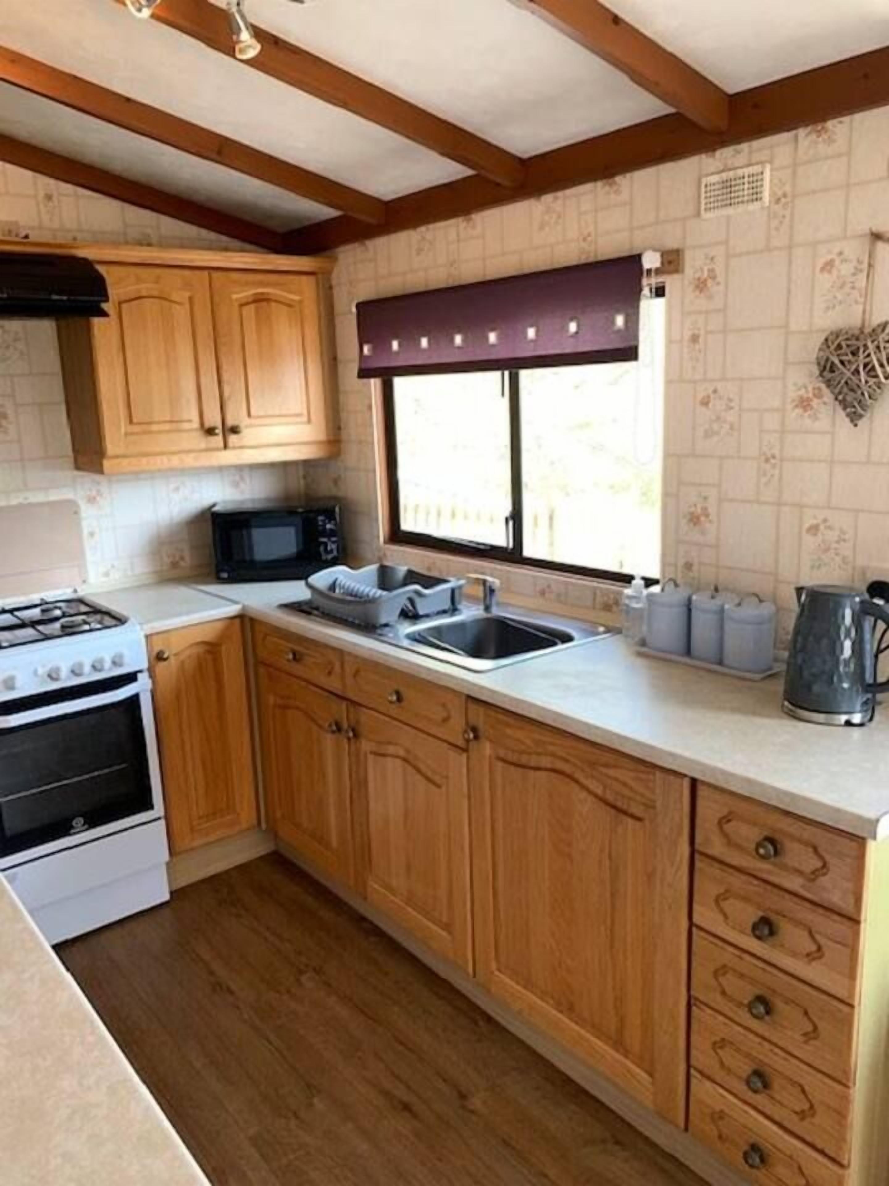 Una cocina compacta con armarios de madera, estufa a gas, microondas y ventana con cortina.