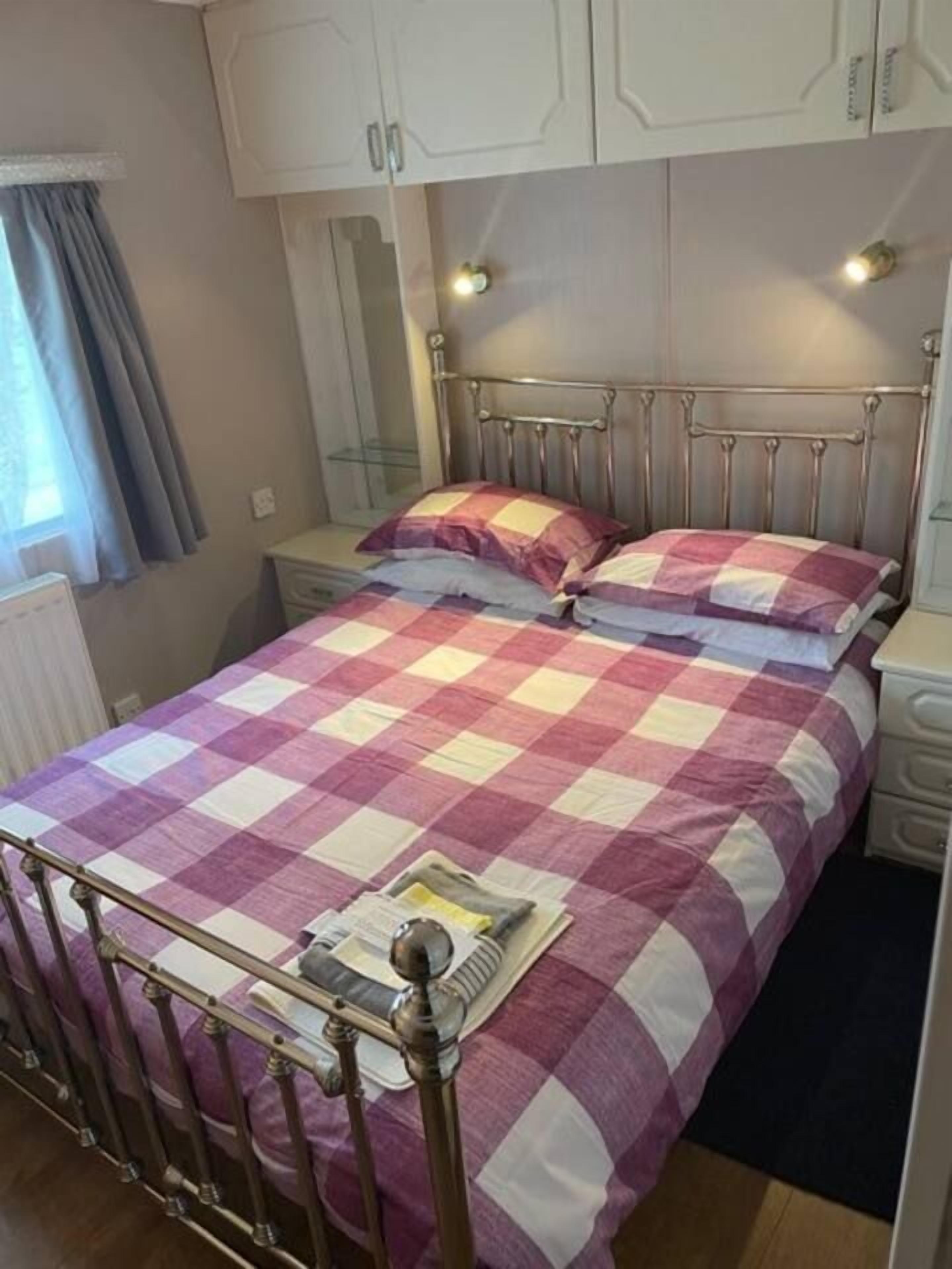 A single bed with a metal frame, a checkered bedspread, and a bedside table with a lamp.