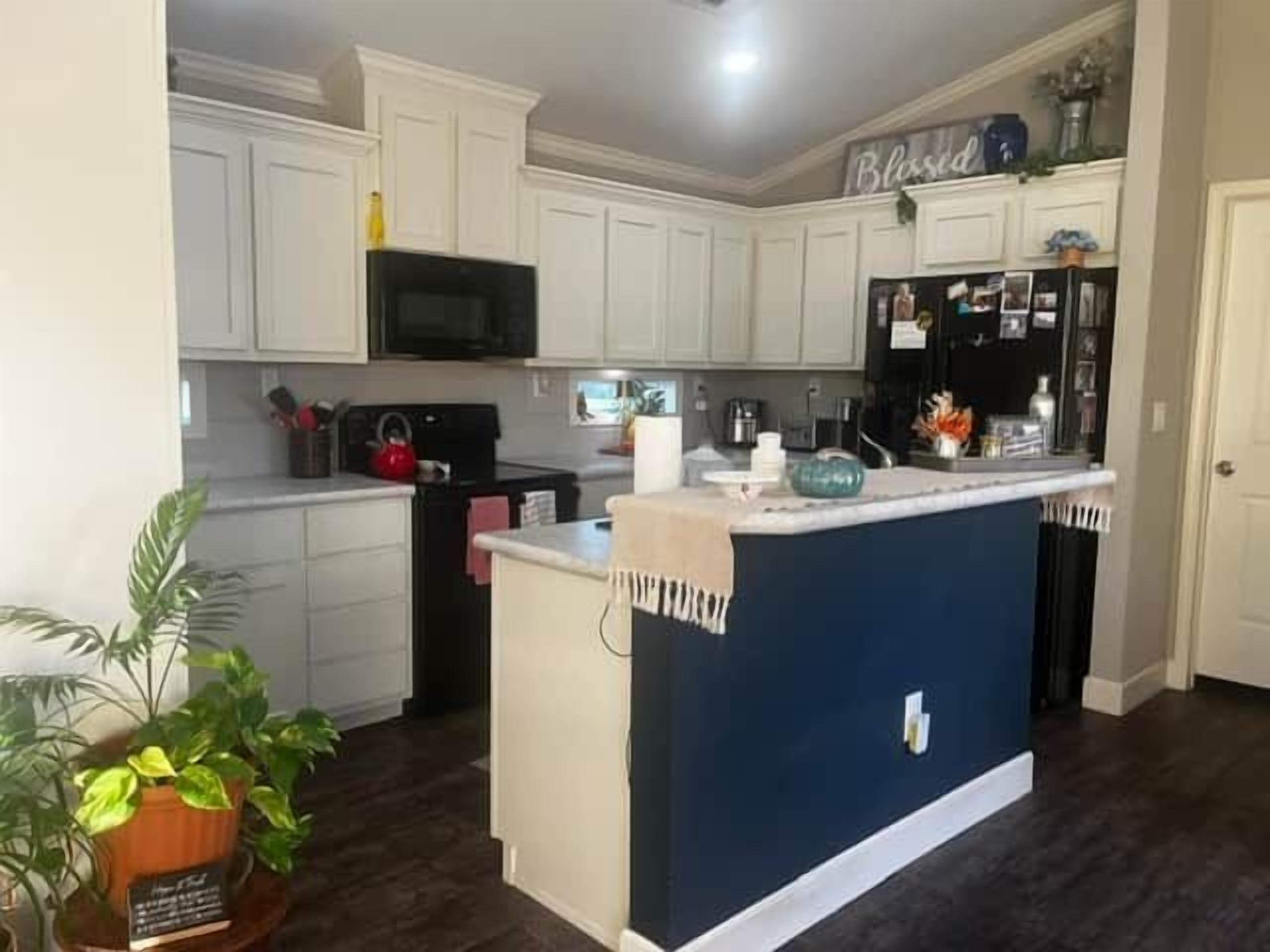 A kitchen with white cabinets, a black microwave, a blue island, and a refrigerator with magnets.
