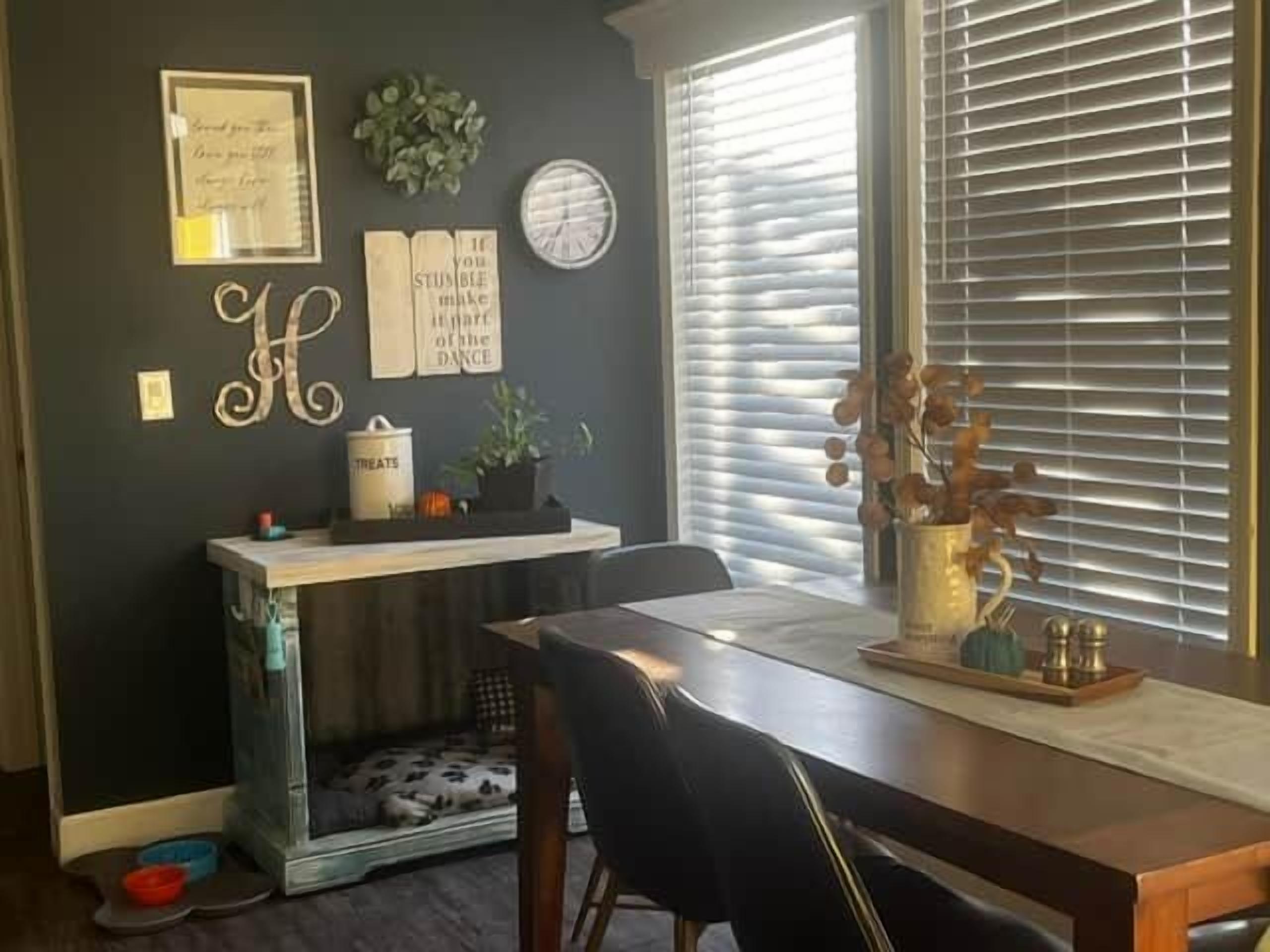 Zona pranzo con tavolo, sedie, cuccia per animali, una pianta e una finestra con persiane.