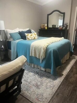 A bedroom with a bed, bedside table, lamp, dresser, mirror, and a chair.