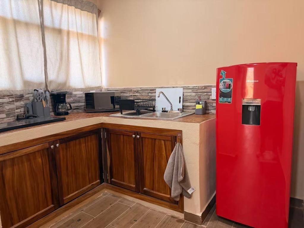 Una cocina con armarios de madera, un refrigerador rojo, una cafetera y un lavamanos.