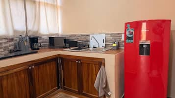 Una cocina con armarios de madera, un refrigerador rojo, una cafetera y un lavamanos.