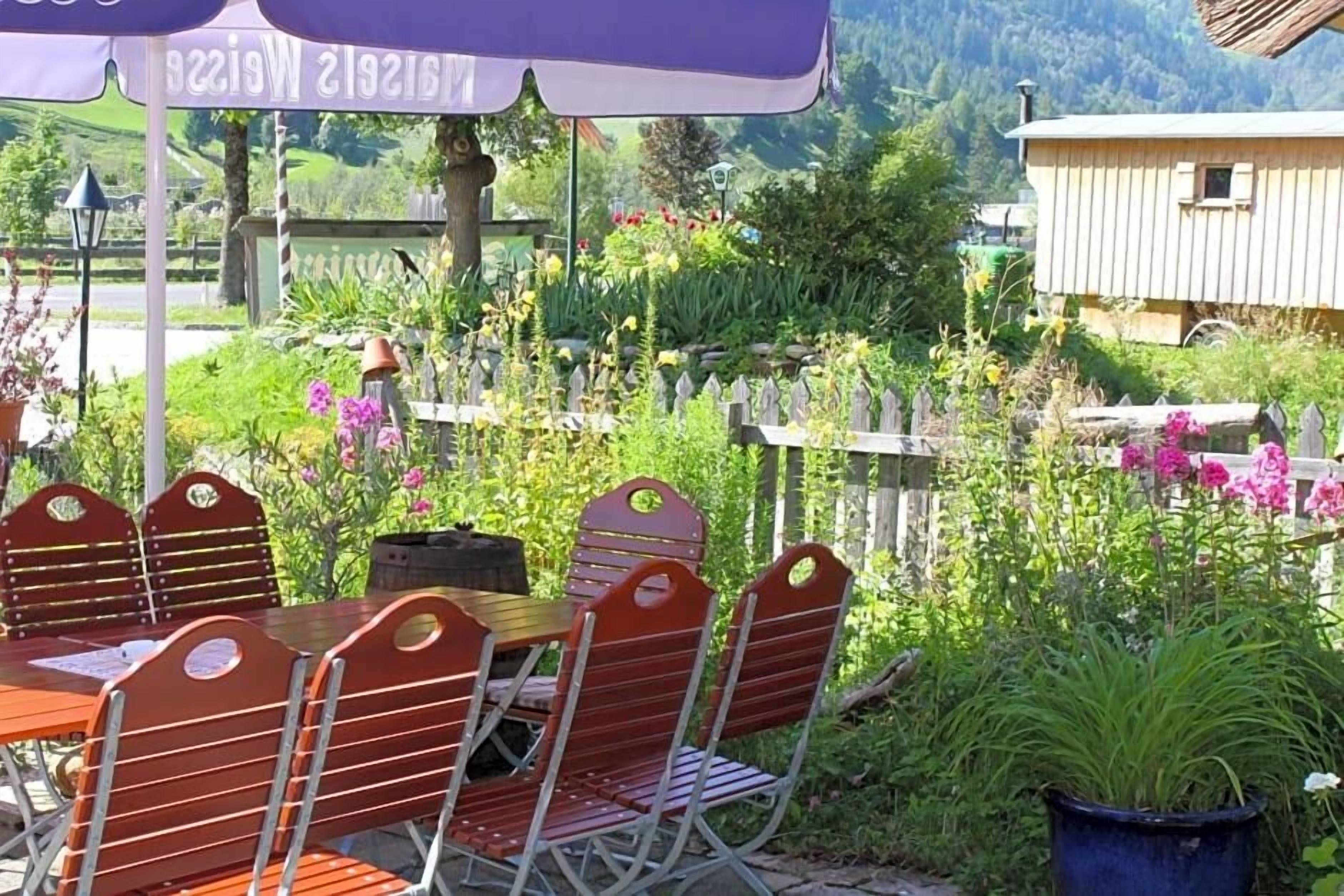 An outdoor seating area with a table and chairs, surrounded by a wooden fence and various plants.