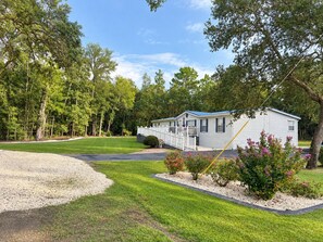 Une maison mobile dotée d’un porche à l’avant, entourée d’une pelouse bien entretenue et d’arbres.