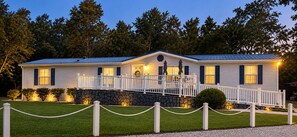 Ein zweigeschossiges Haus mit Natursteinfundament, einer Veranda mit Geländer und einem kleinen Vorgarten.