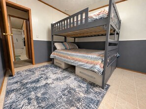 Ein Stockbett mit gestreifter Bettdecke, einer kleinen Schublade und einem gemusterten Teppich.