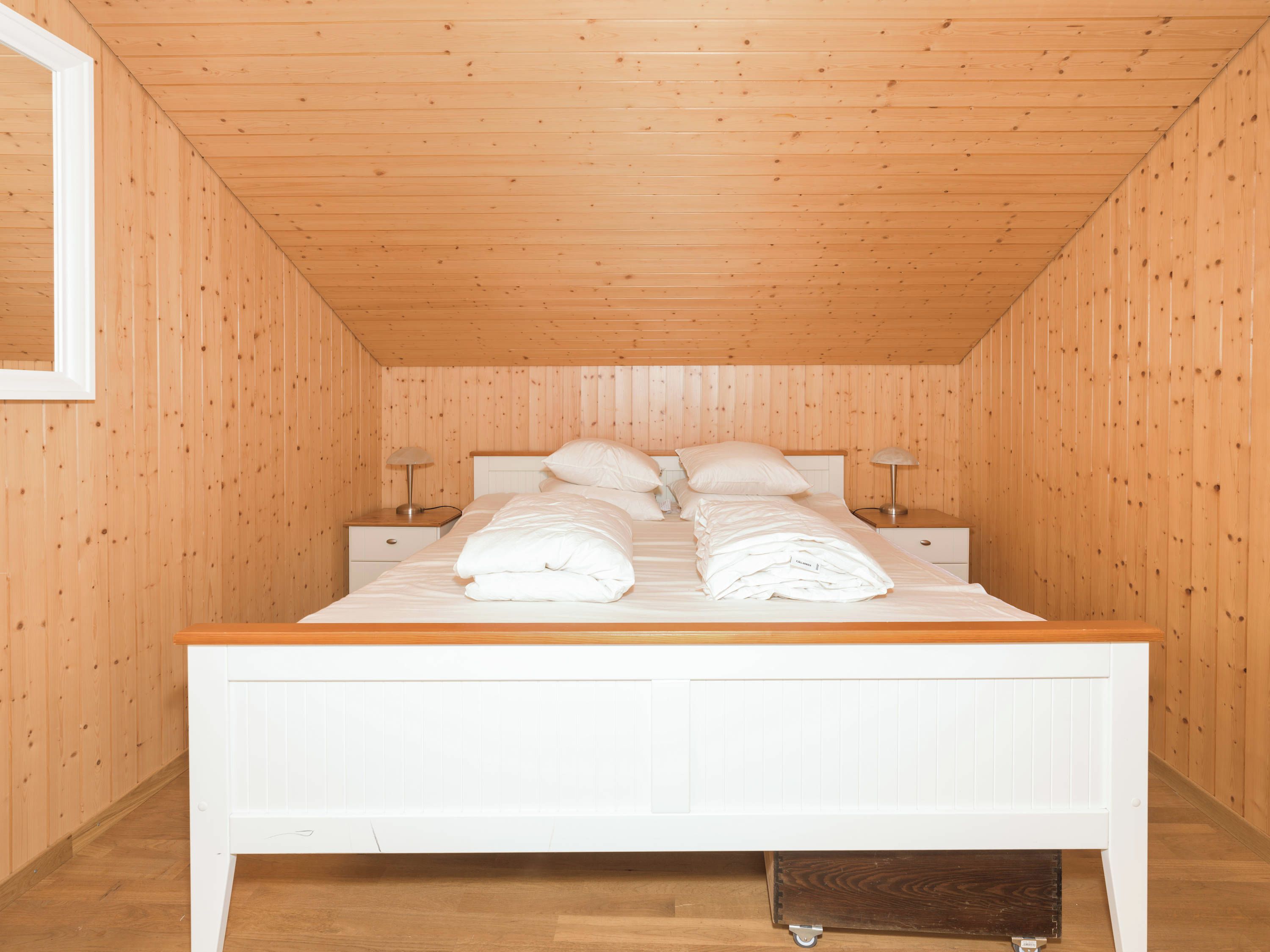 A bedroom with a wooden ceiling, a white bed, and two bedside tables with lamps.