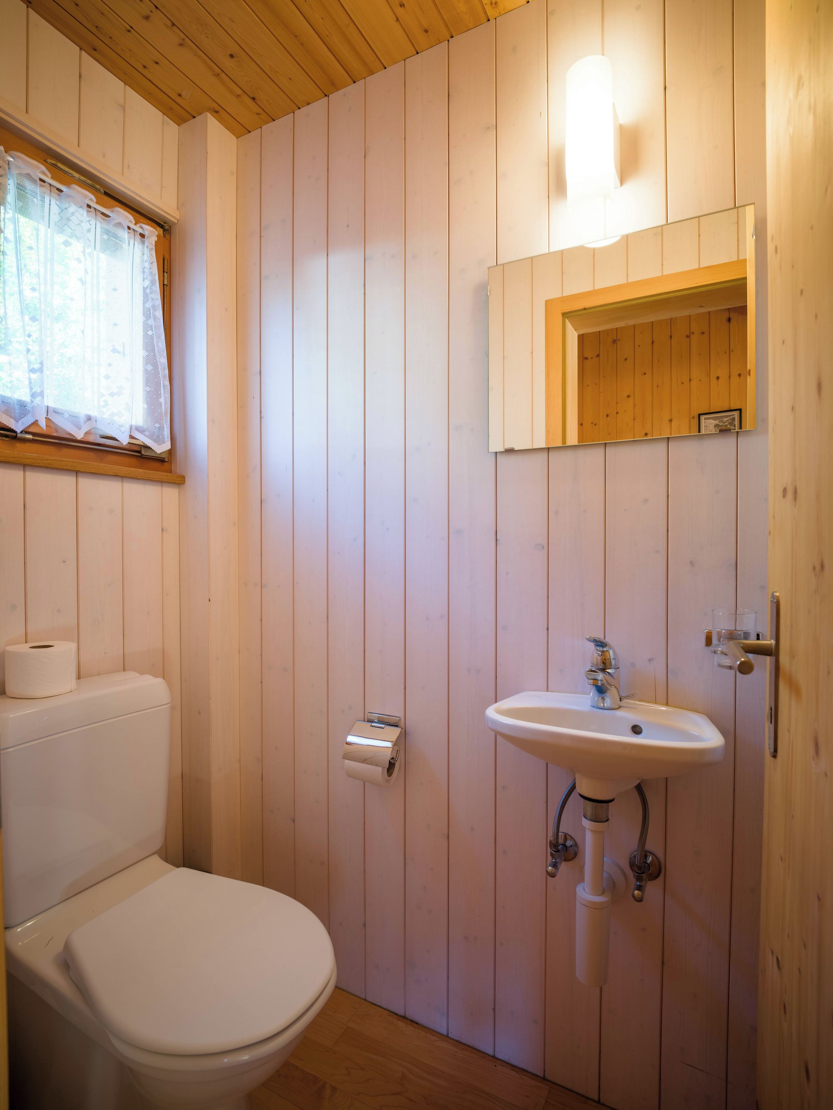 Een betegelde badkamer met toilet, wc-papier, wastafel en spiegel.