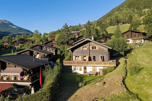 Un grupo de chalets de madera con techos inclinados, ubicados en una zona montañosa con abundante vegetación y cielo despejado.