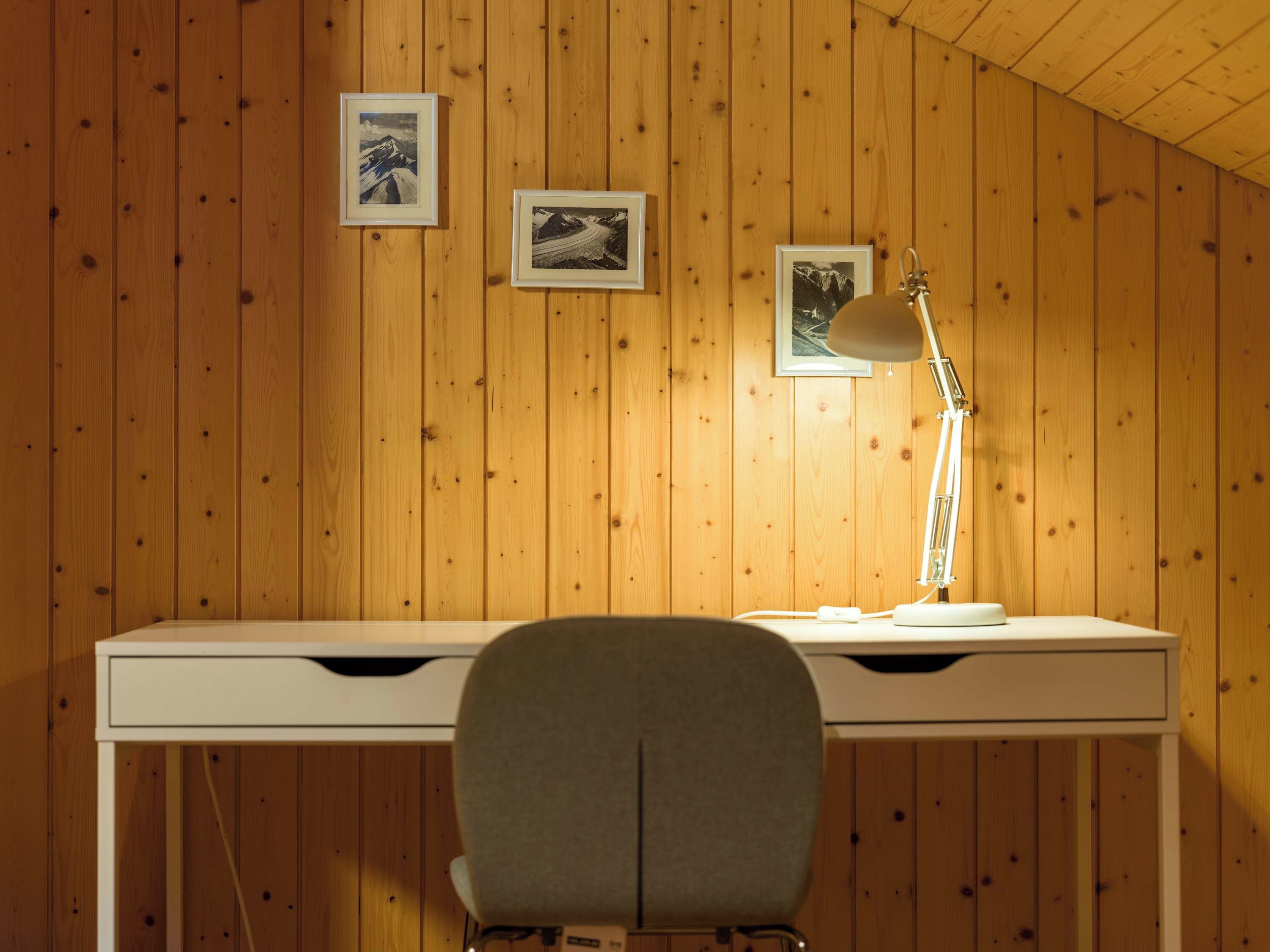 A wooden-paneled room with a desk, a chair, and three framed photographs on the wall.