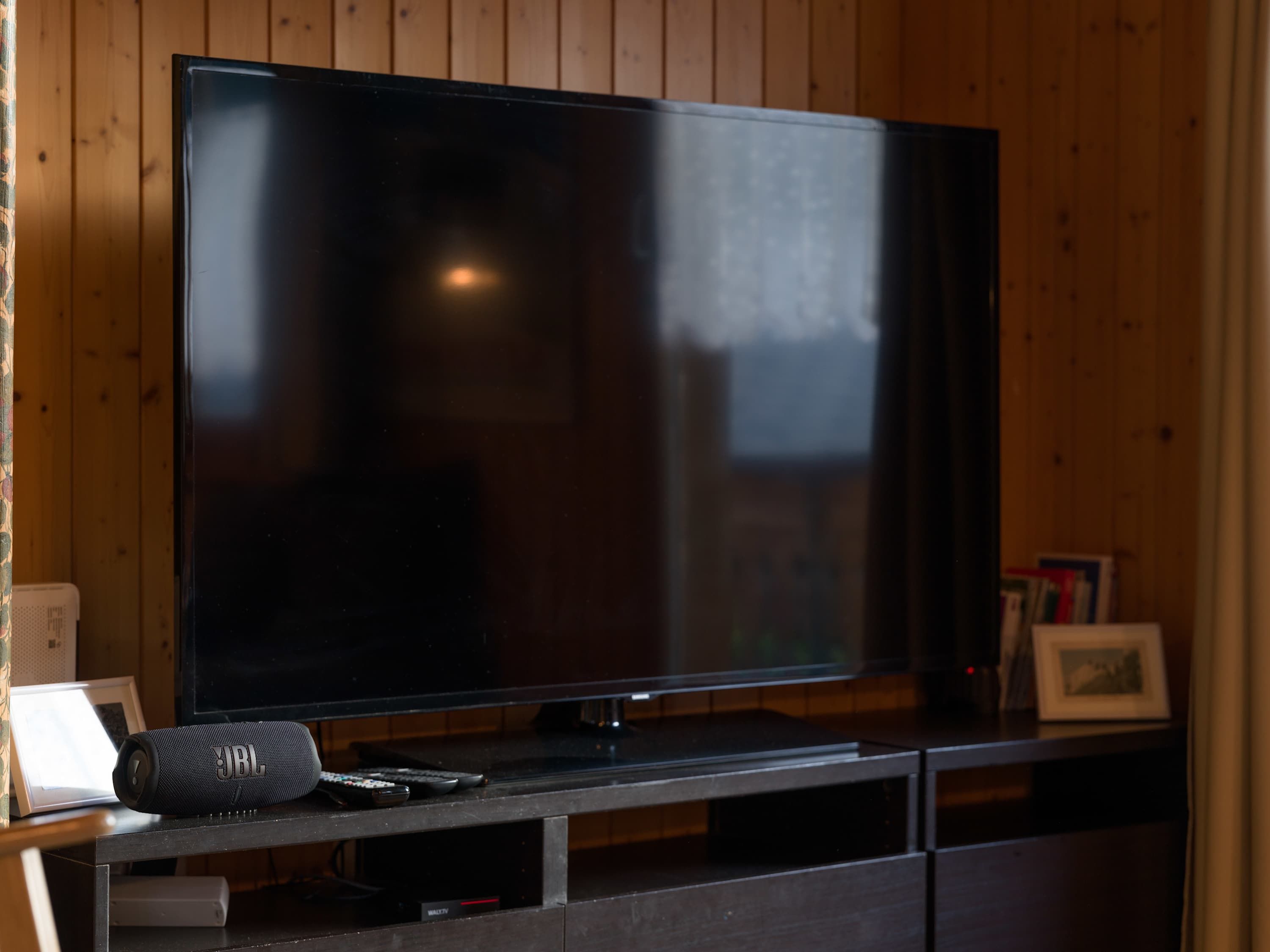 Ein Flachbildfernseher auf einer Holztruhe mit einem JBL Lautsprecher und Fernbedienung.