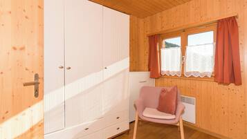 Ein Zimmer mit Holzwänden, einem weißen Kleiderschrank, einem rosa Stuhl und einem Fenster mit Vorhängen.