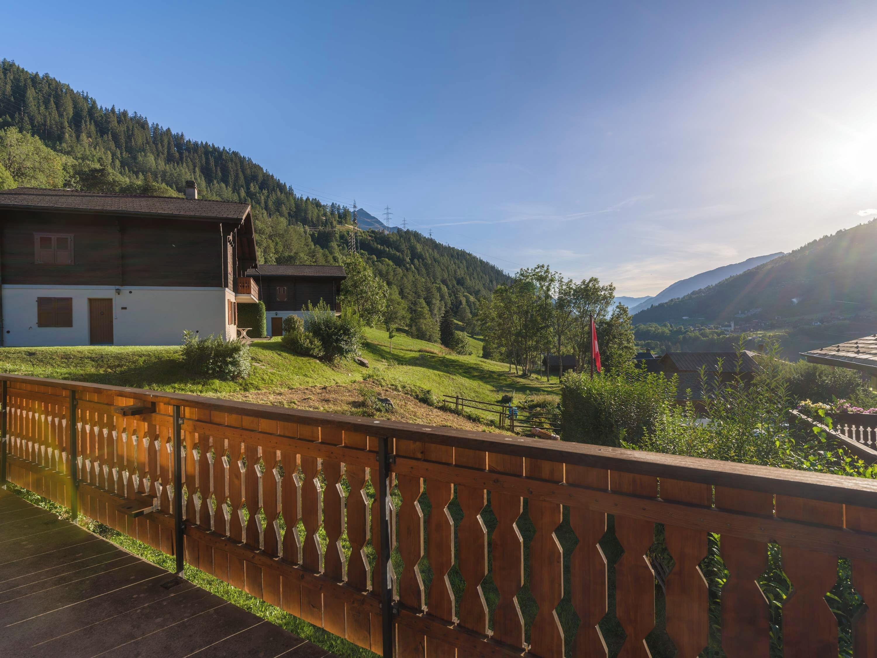 A wooden fence with a decorative pattern, a building with a sloped roof, and a mountainous landscape in the background.