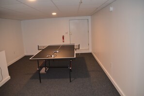 A room with a ping pong table, a door, and a fire extinguisher on the wall.