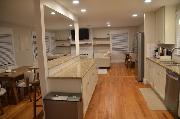 A modern kitchen with a central island, wooden flooring, built-in appliances, and a dining area with chairs.