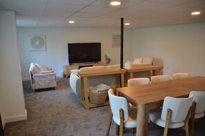 A living room with a television, a sofa, a dining table with chairs, and a carpeted floor.