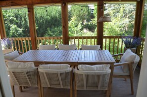 A wooden deck with a table and chairs, surrounded by greenery.