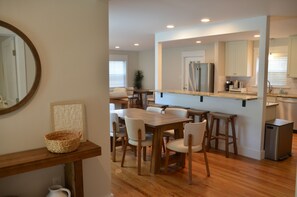A modern kitchen with wooden cabinetry, a stainless steel refrigerator, and a dining area with a wooden table and chairs.