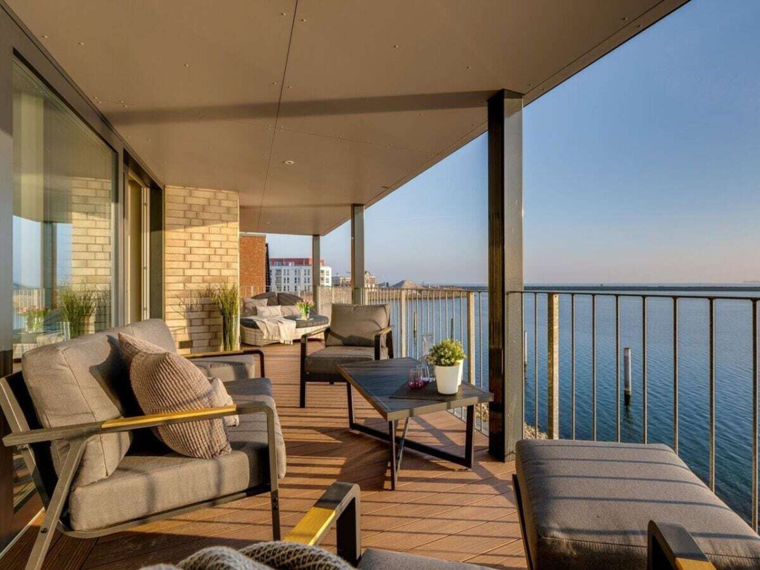 A balcony with a view of the sea, furnished with a sofa, chairs, and a table.