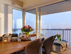 Ein Essbereich mit Meerblick, ein Holztisch mit Tellern und einer Blumenvase, sowie ein Balkon mit Geländer.