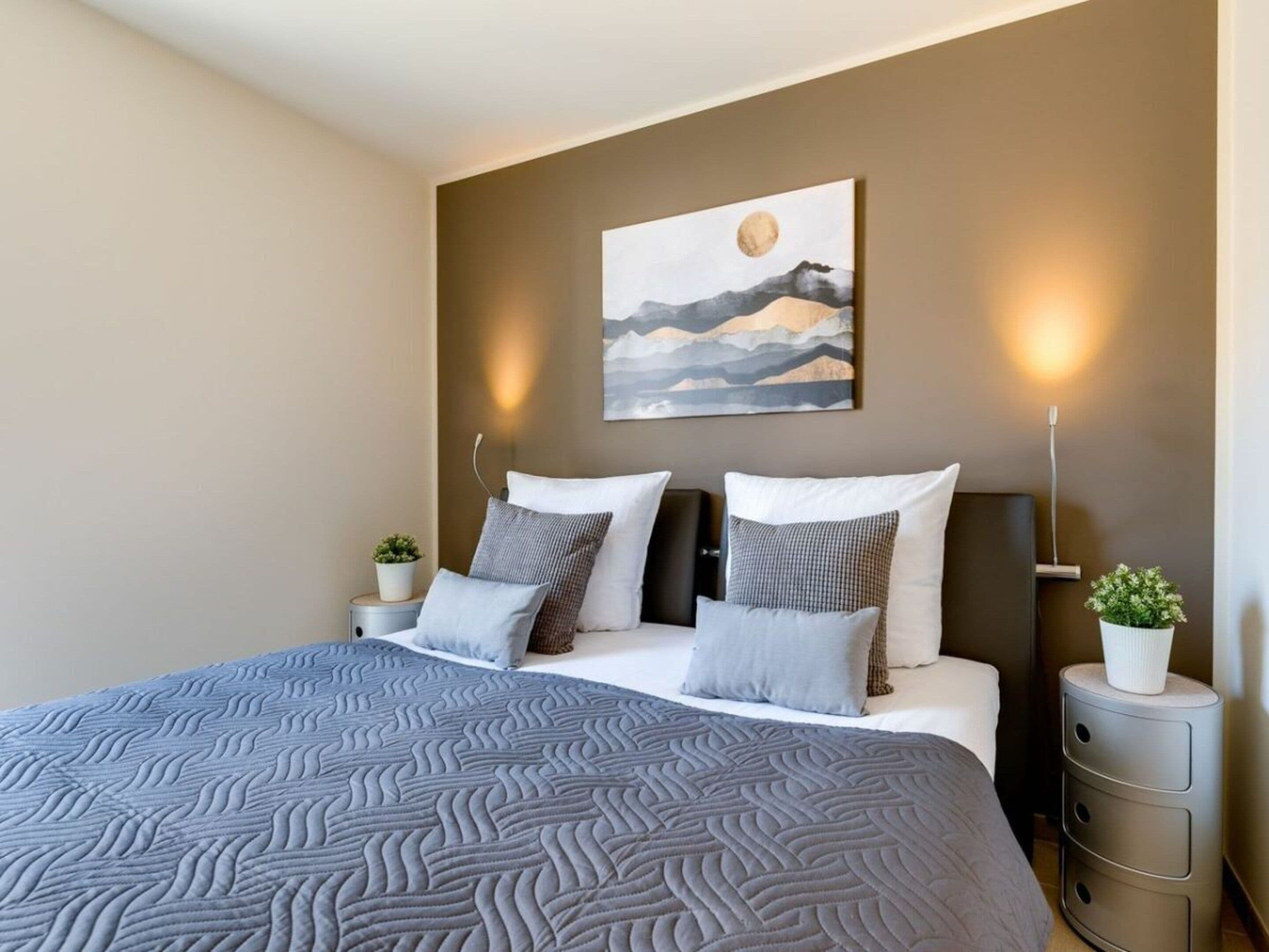 A modern bedroom with a large bed, a wall-mounted painting, bedside lamps, and a small plant on the nightstand.