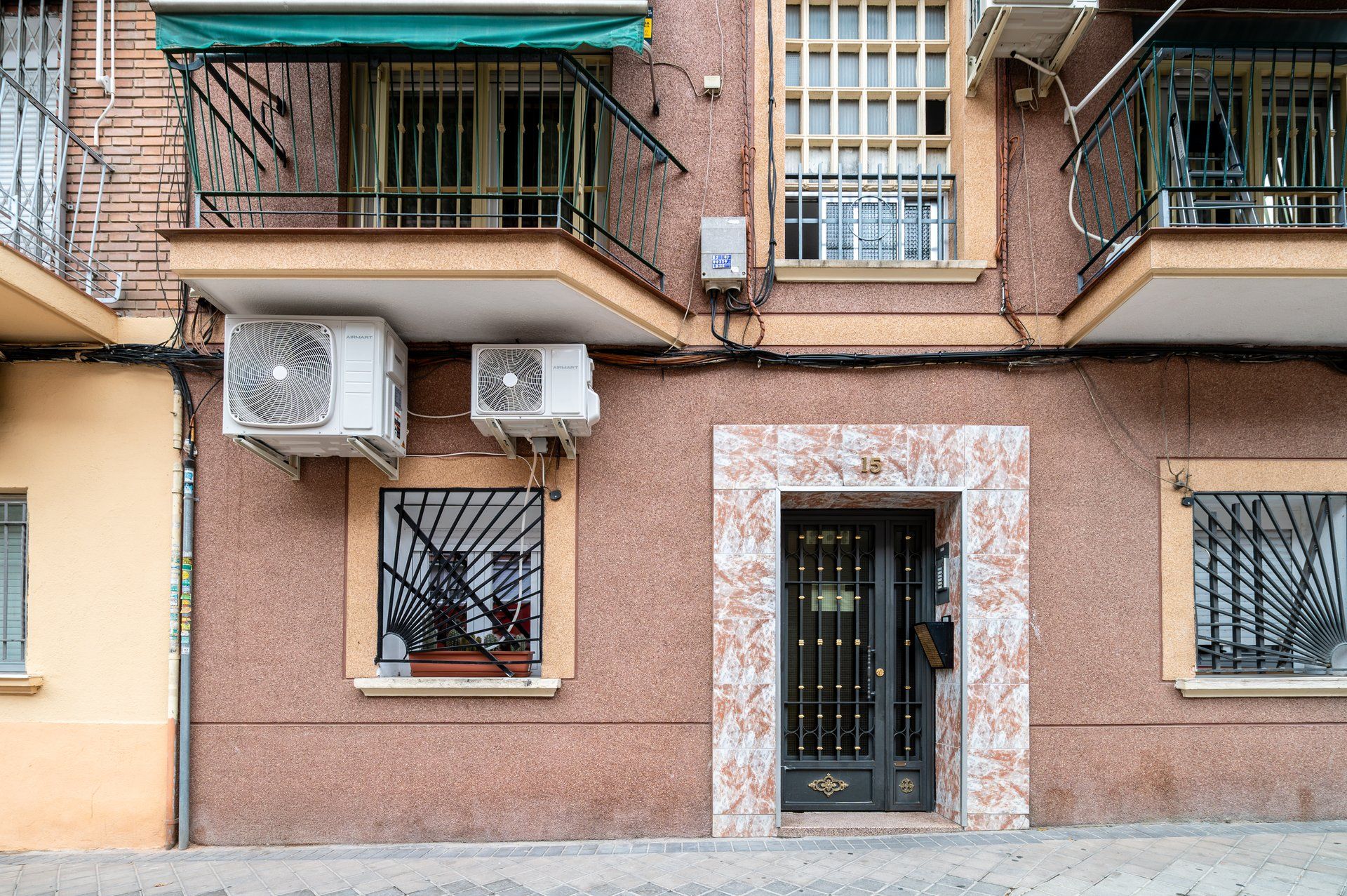 A building with multiple air conditioning units, a black door with a decorative grille, and a number '15' above the door.