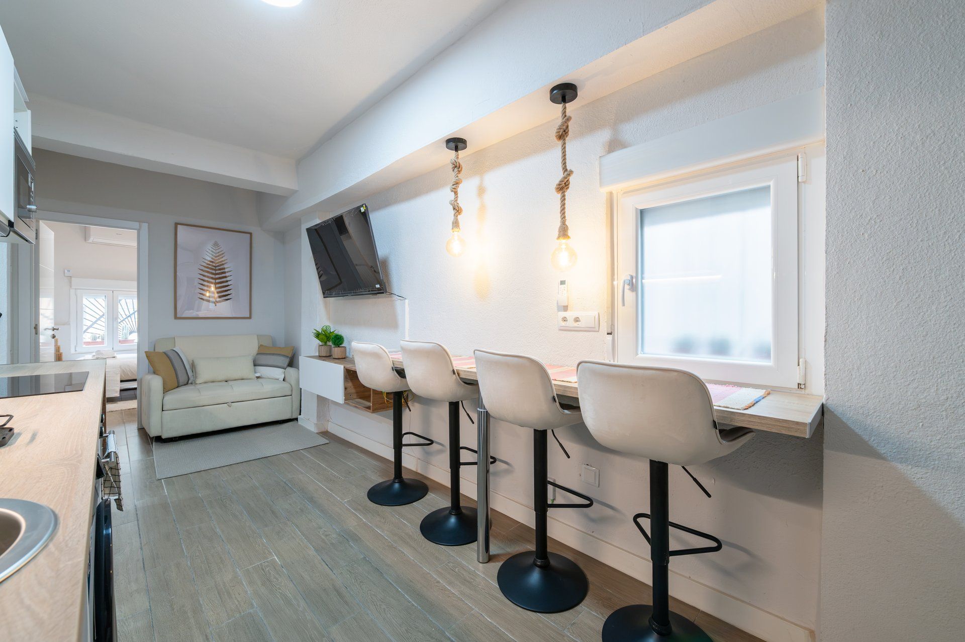 A modern kitchen with a dining area, bar stools, and a large window.