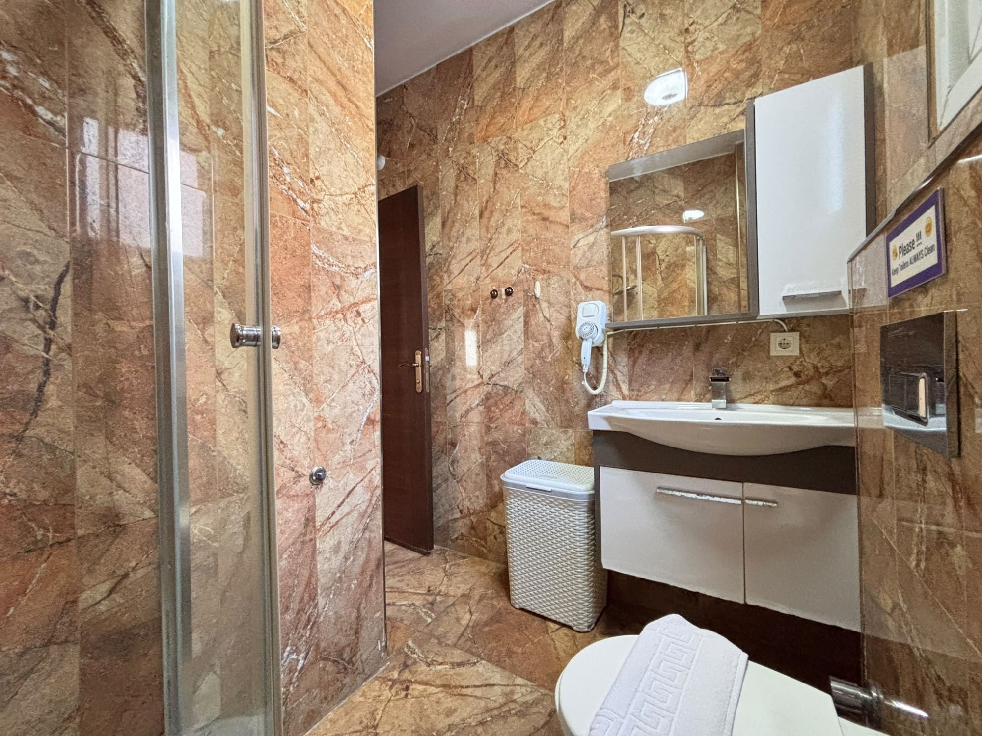 Casa de banho com cabine de chuveiro em vidro, lavatório branco, espelho e lixeira.