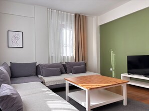 A modern living room with a grey sofa, a wooden coffee table, a television on a white stand, and a green accent wall. - Central 3BR Near Metro and Cevahir (Istanbul)