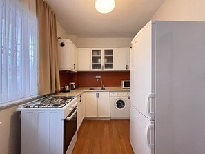 A compact kitchen with a gas stove, oven, microwave, sink, and a washing machine. - Central 3BR Near Metro and Cevahir (Istanbul)