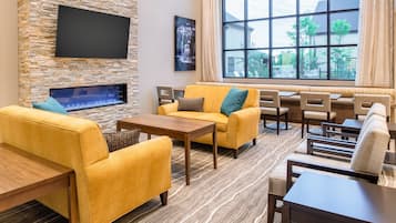 A modern lounge area with a stone wall, flat-screen TV, fireplace, yellow sofas, and a large window offering a view of the outdoors.