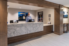 A reception desk with a marble counter, a digital kiosk, and a framed landscape painting.