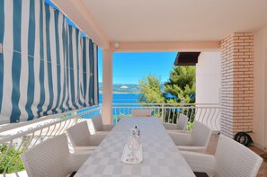 Une terrasse avec une table à carreaux, des chaises en osier blanches, un auvent rayé et une vue sur la mer.