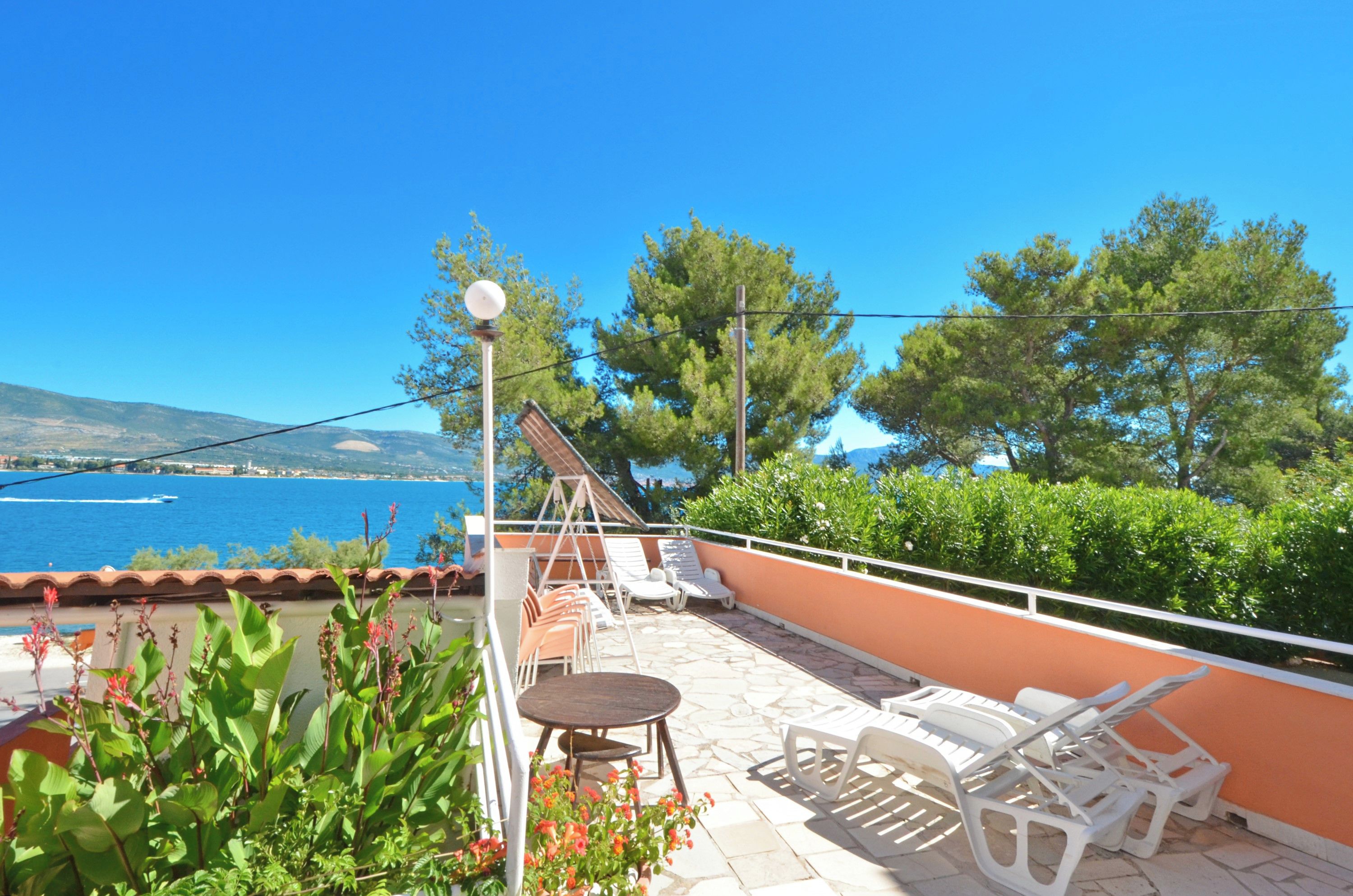 A terrace with a table and chairs, overlooking a body of water and a mountainous landscape.
